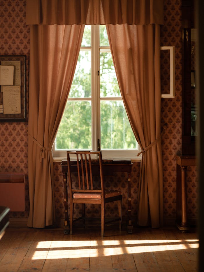 A cozy vintage room with a wooden chair and table by a window with curtains.