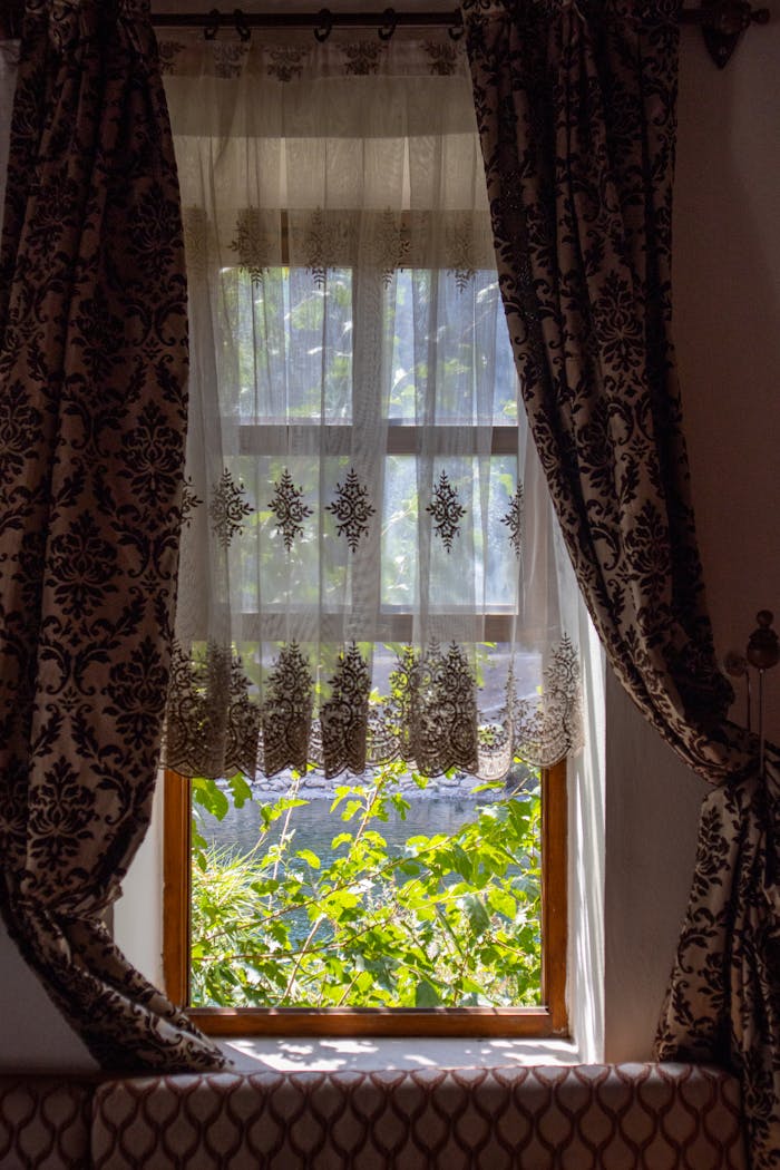 A beautifully adorned window in Palu, Türkiye with sunlight filtering through sheer, patterned curtains.