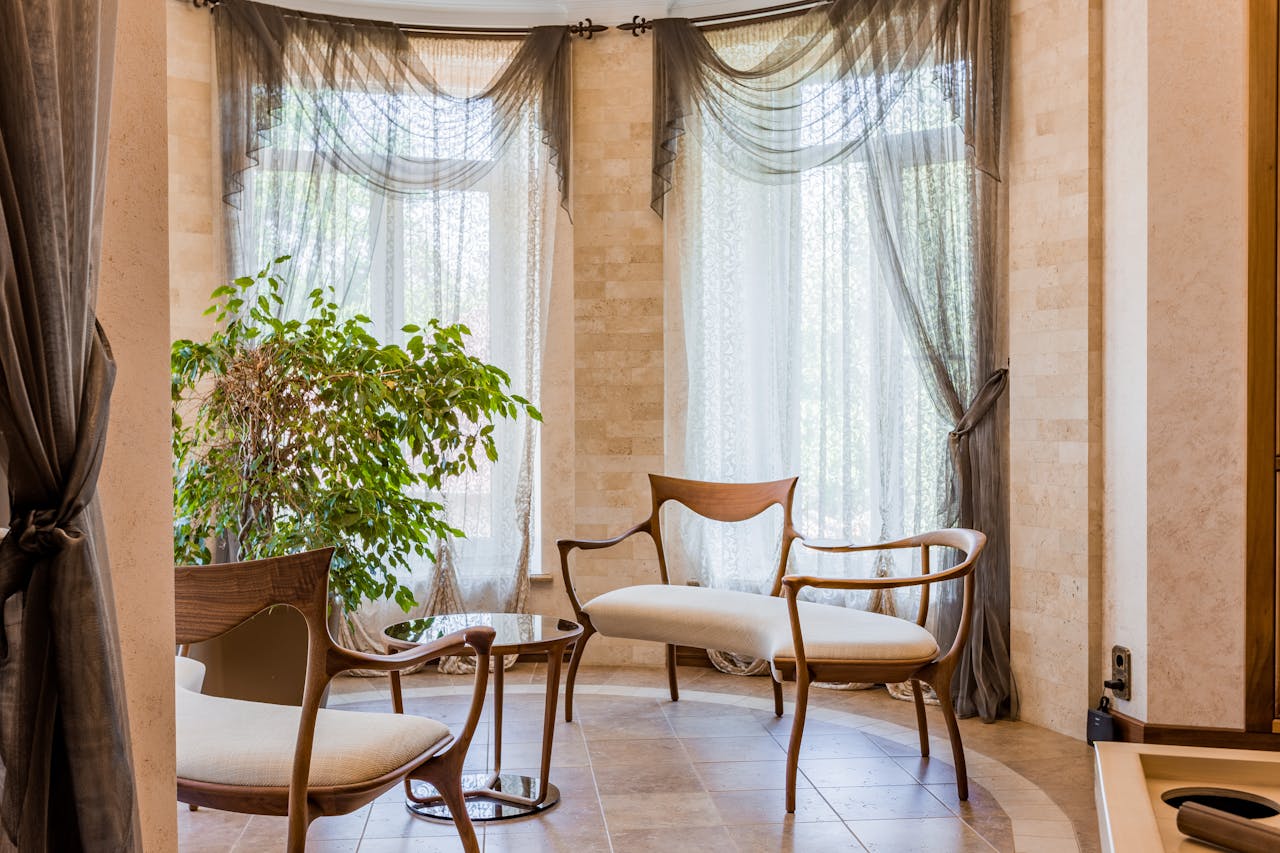 Stylish seating area with elegant wooden chairs and flowing curtains in a bright room.