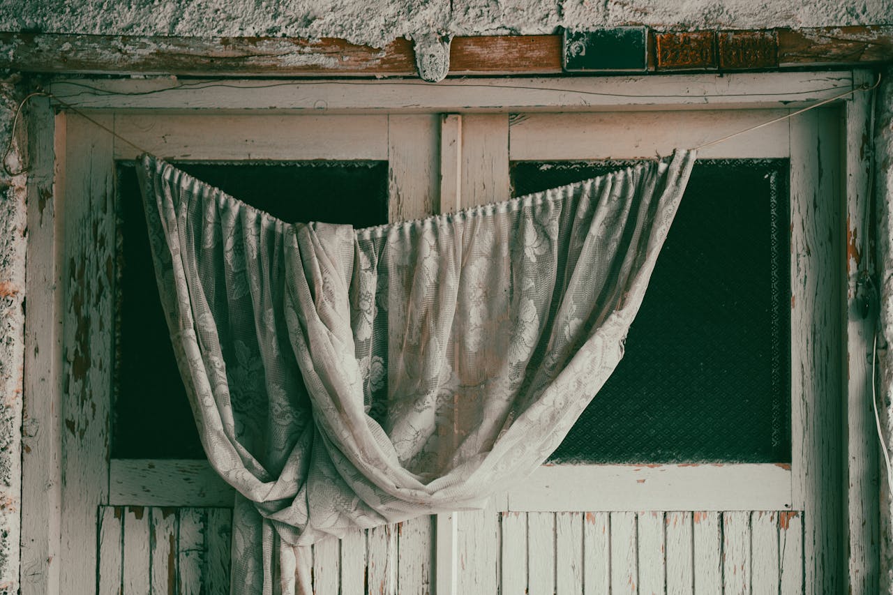 An elegant vintage curtain draped over an aged wooden door evokes a nostalgic, rustic charm.