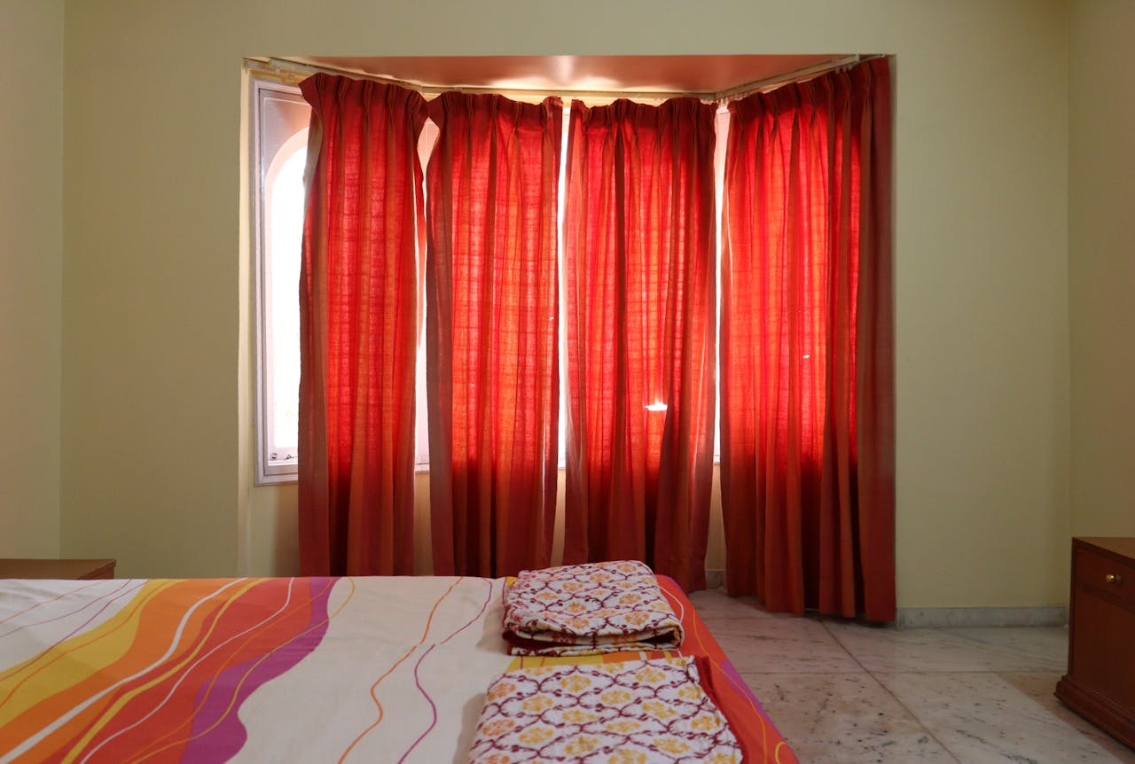 A cozy bedroom showcasing red curtains and a colorful bedspread, creating a warm ambiance.