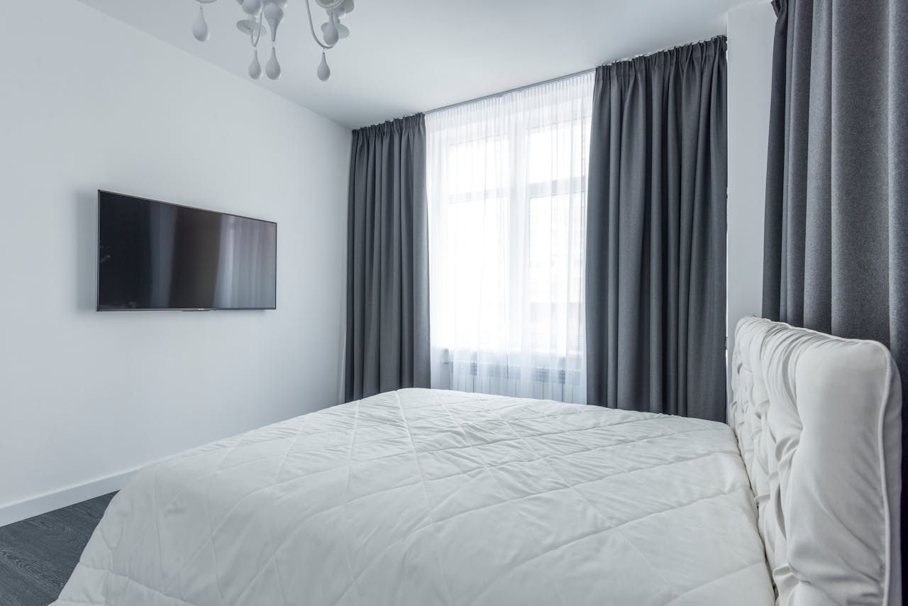 A modern bedroom featuring minimalist decor with a flat-screen TV and elegant curtains.